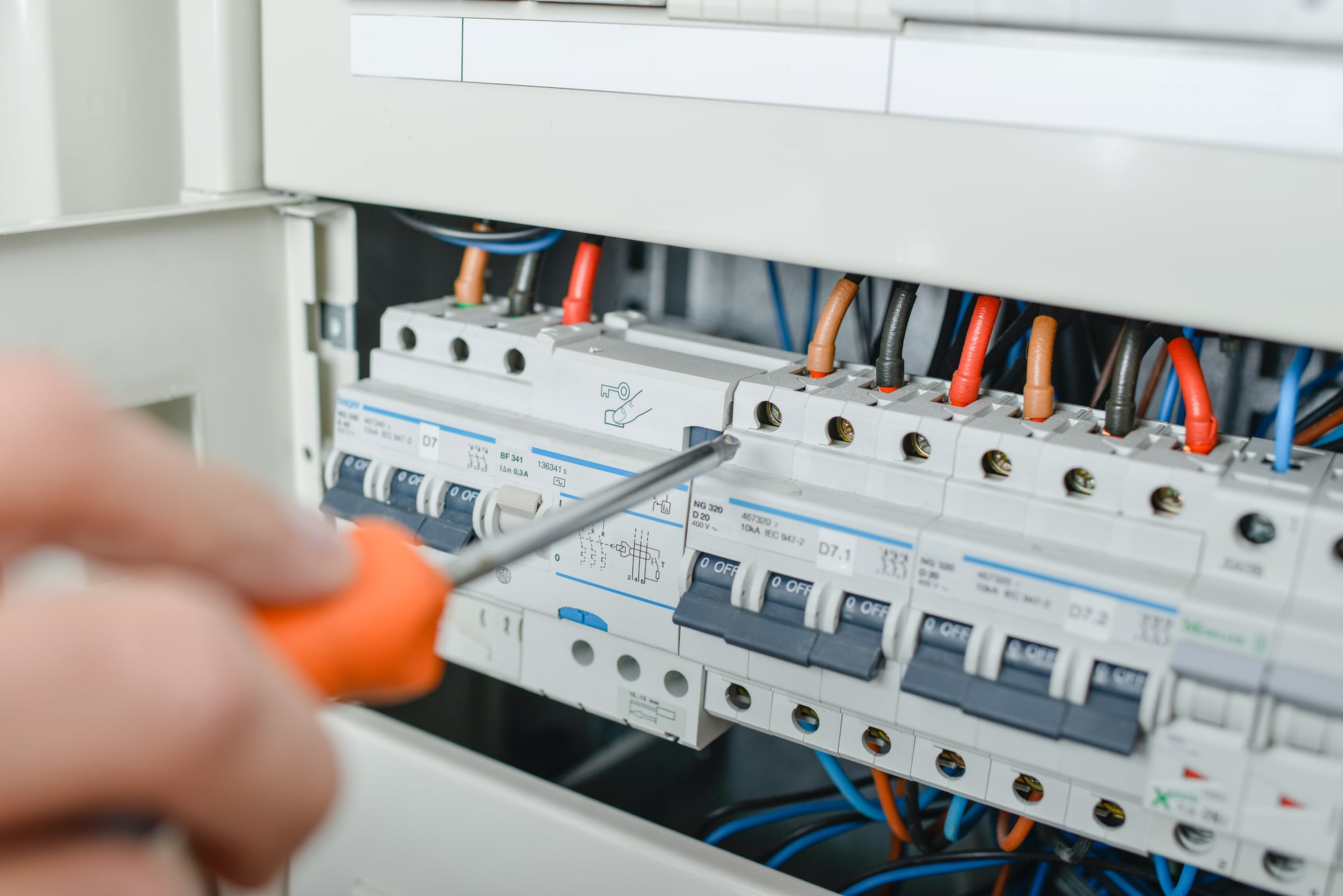 An electricians hand holding a screwdriver as he unscrews a breaker from the breaker panel